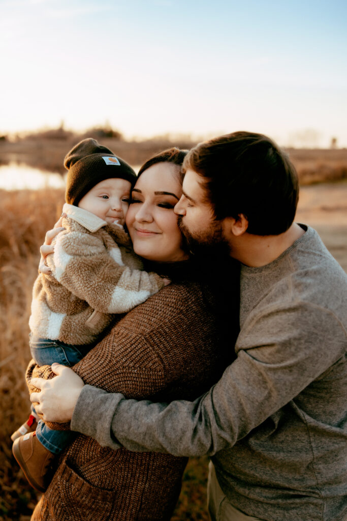 Parents with young baby wearing brown and cream clothing at a family photoshoot in the springtime when the landscape is dead.