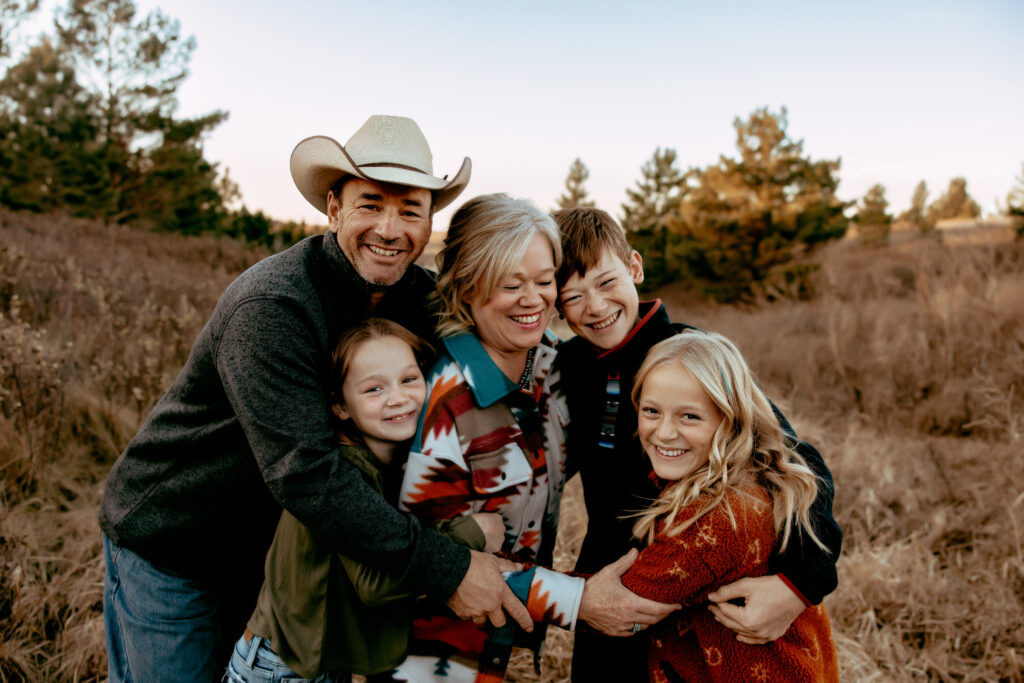 A family of five embracing in a brown field wearing colorful clothing to make them pop against the landscape during a spring family photoshoot.
