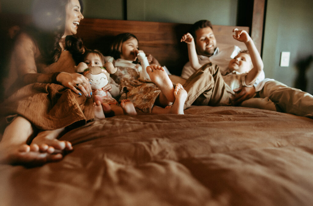 Family laying together on the bed cuddling and telling stories during an in-home family photography session.