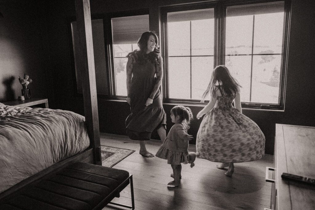 Black and white photo of two little girls dancing with their mom and twirling their dresses.